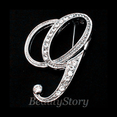 Silver brooch with intricate design letter G on a black background, branded 'BeautyStory'.