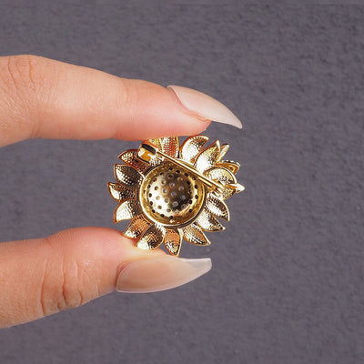 the back of a Gold sunflower-shaped brooch held between fingers against a gray background