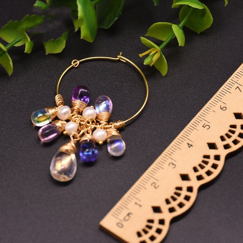 Gold hoop earring with colorful beads and pearls on a dark surface with a ruler for scale.