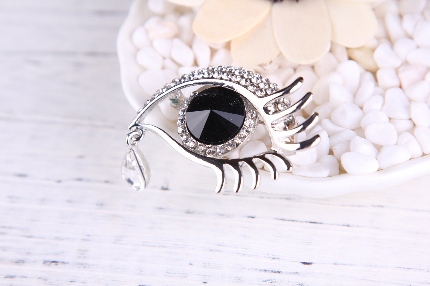 Silver eye-shaped brooch with a black gemstone on a white background