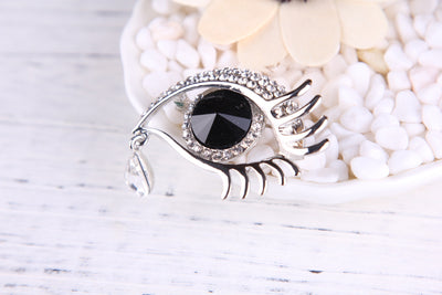 Silver eye-shaped brooch with a black gemstone on a white background