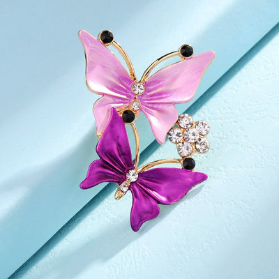Butterfly-shaped brooch with pink and purple wings on a light blue background