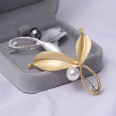silver and a Gold leaf-shaped brooch with pearl and gemstone on a gray jewelry box