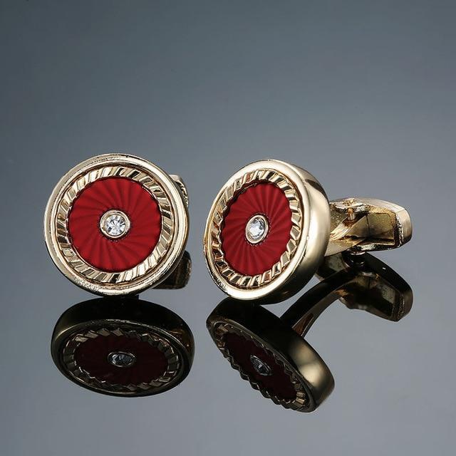 Gold cufflinks with red center and diamond-like stone on a reflective surface.