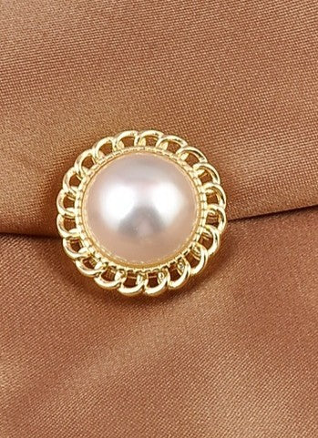 Pearl magnetic brooch close up  with gold decorative border on a brown fabric background