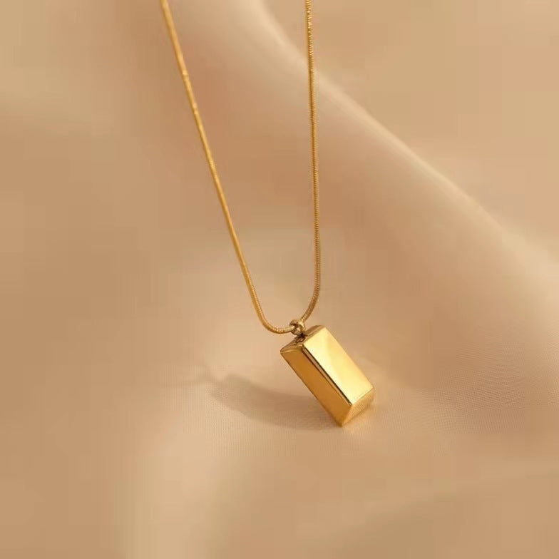 Gold necklace with a rectangular pendant on a beige background