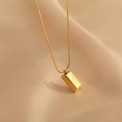 Gold necklace with a rectangular pendant on a beige background