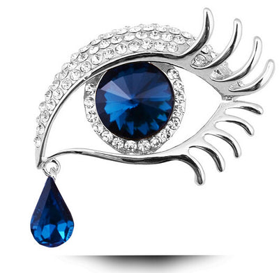 Eye-shaped brooch with blue gem and teardrop accent on a white background