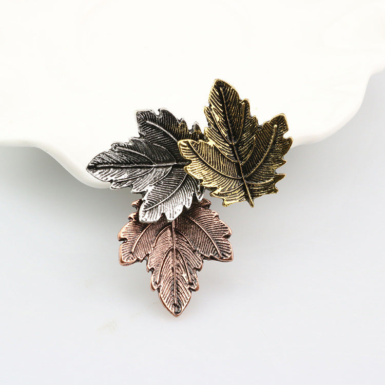 Three leaf-shaped pins in silver, gold, and bronze on a white background