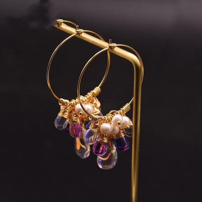 Gold hoop earrings with pearls and purple beads on a dark background