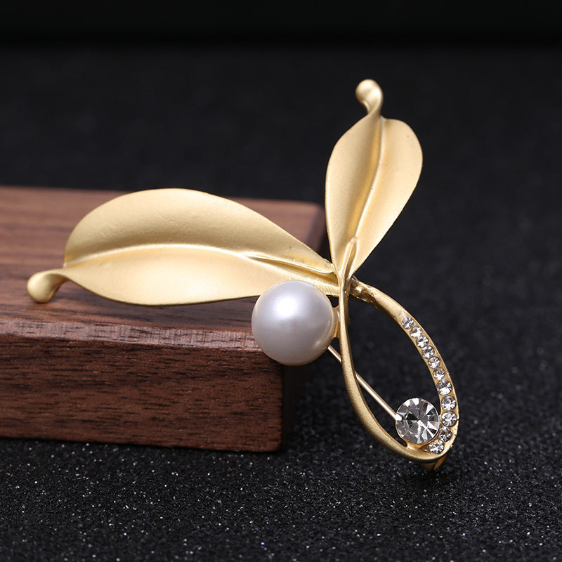 Gold leaf-shaped brooch with a pearl and gemstone on a dark background