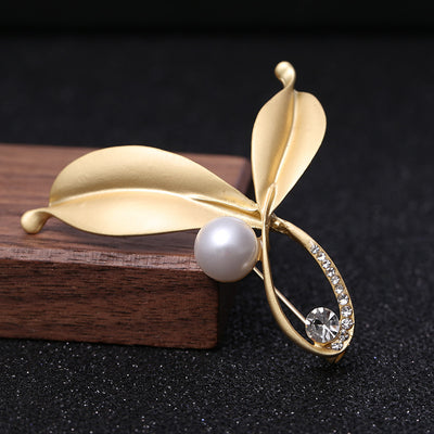 Gold leaf-shaped brooch with a pearl and gemstone on a dark background