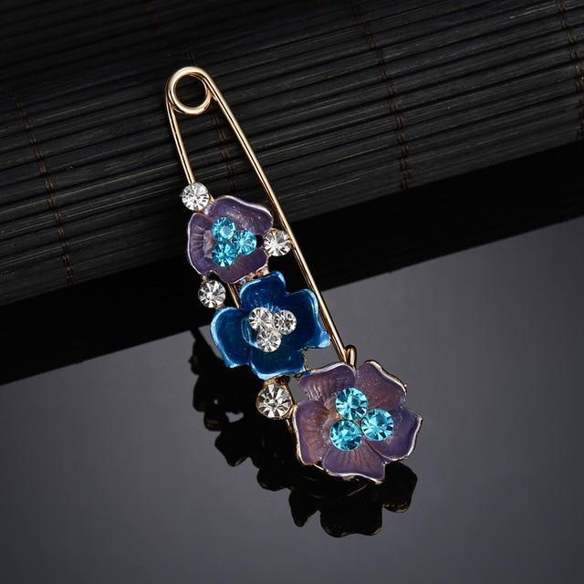 Floral brooch with blue and purple flowers on a reflective surface