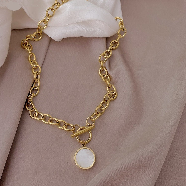 Gold chain bracelet with a round charm on a soft pink fabric background