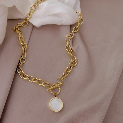 Gold chain bracelet with a round charm on a soft pink fabric background