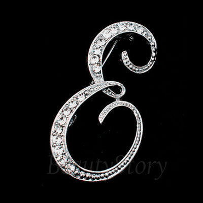 Silver brooch with intricate design  letter E on a black background