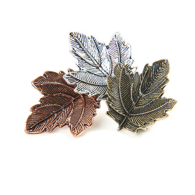 Three leaf-shaped pins in bronze, silver, and gold on a white background