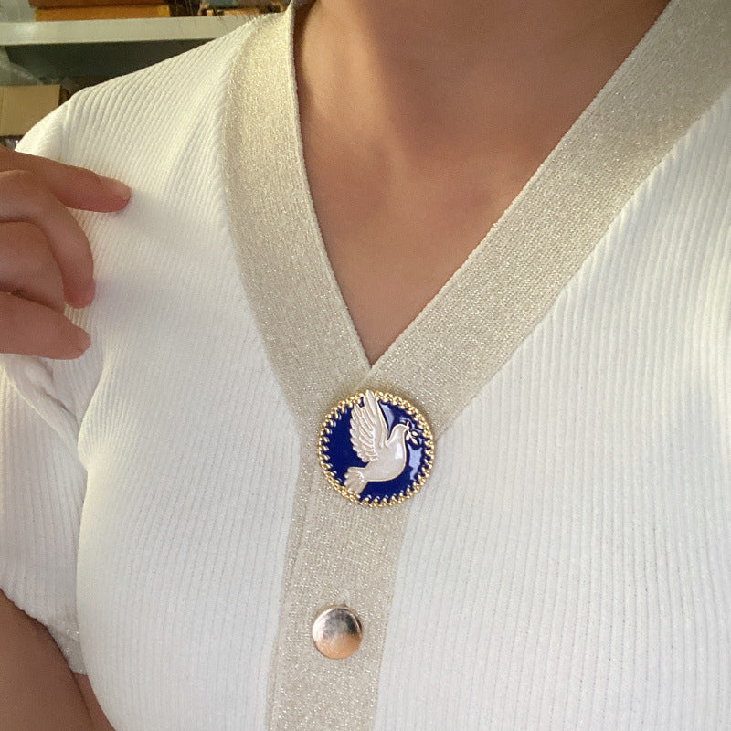 Person wearing a white sweater with a decorative brooch featuring a dove design.