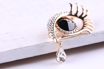 Gold eye-shaped brooch with black center and teardrop-shaped pendant on a white surface