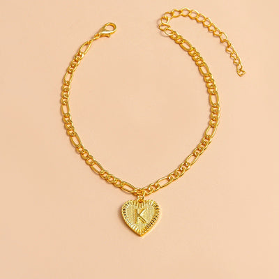 Gold chain necklace with a heart-shaped pendant featuring the letter 'K' on a beige background