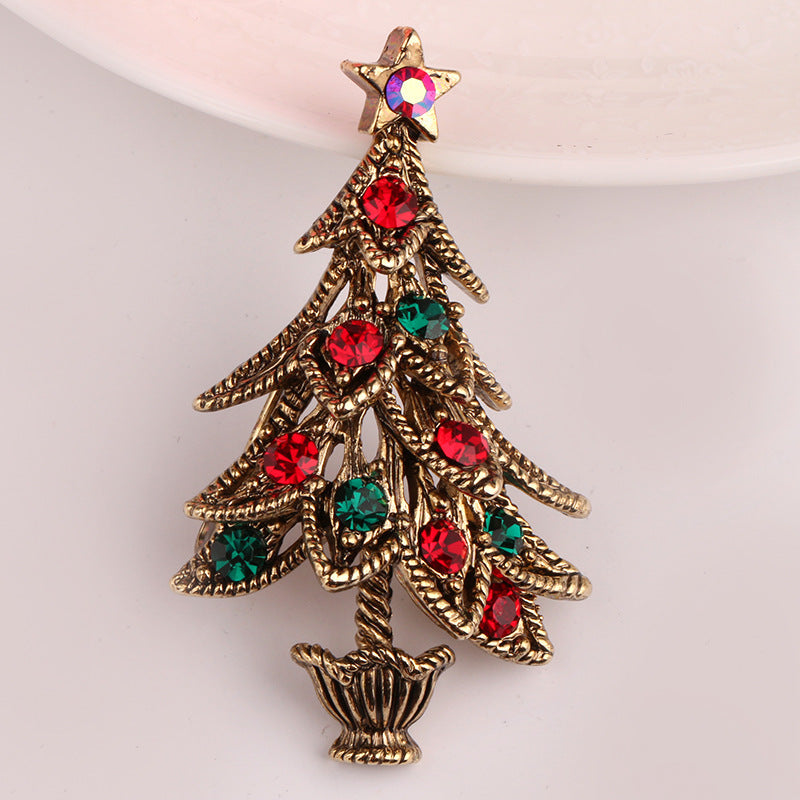 Christmas tree-shaped brooch with red and green gemstones on a light pink background
