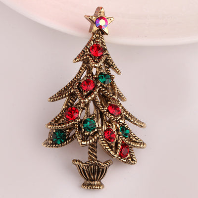 Christmas tree-shaped brooch with red and green gemstones on a light pink background