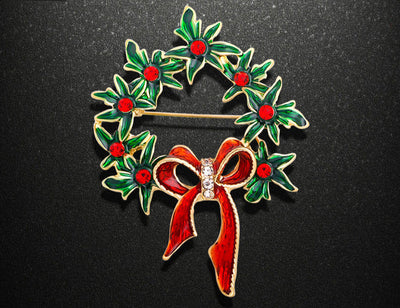 Christmas wreath brooch with red bow and green leaves on a black background