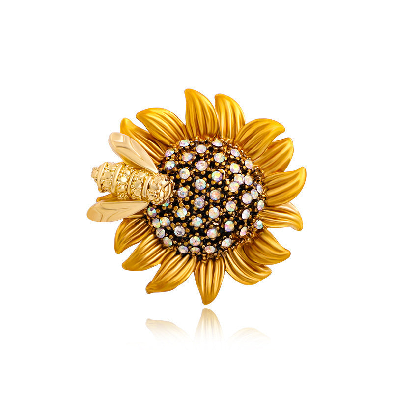 Gold sunflower-shaped brooch with a bee and gemstone center on a white background