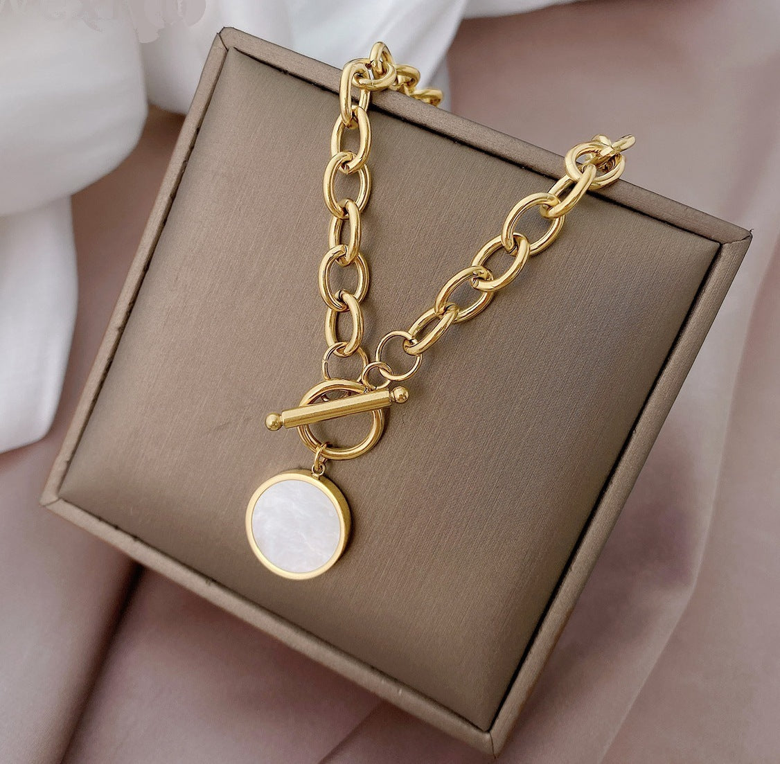 Gold bracelet with a round pendant on a brown jewelry box