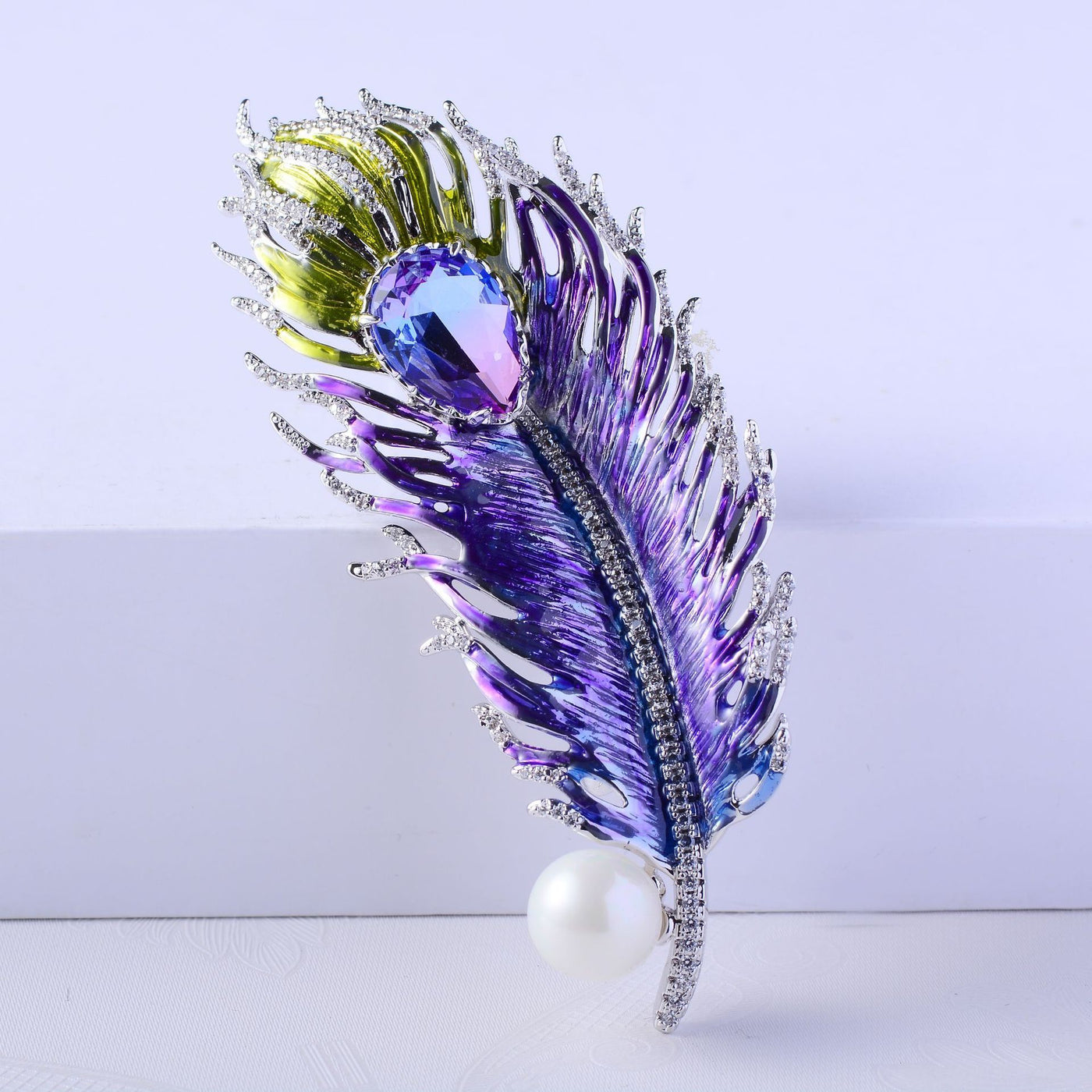 Decorative feather brooch with purple, green, and pearl elements on a light background