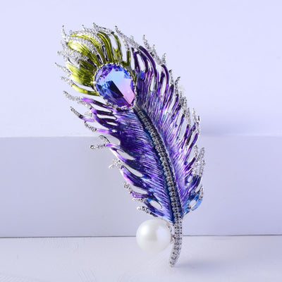 Decorative feather brooch with purple, green, and pearl elements on a light background