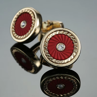 Gold cufflinks with red circular design and diamond center on a reflective surface.