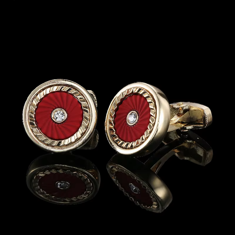 Gold cufflinks with red circular design and diamond center on a black background