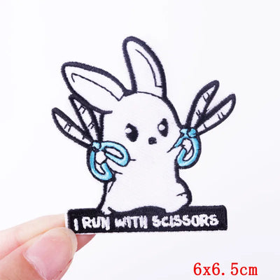 Embroidered patch of a rabbit holding scissors with text 'I Run with Scissors' held by a hand on a white background.