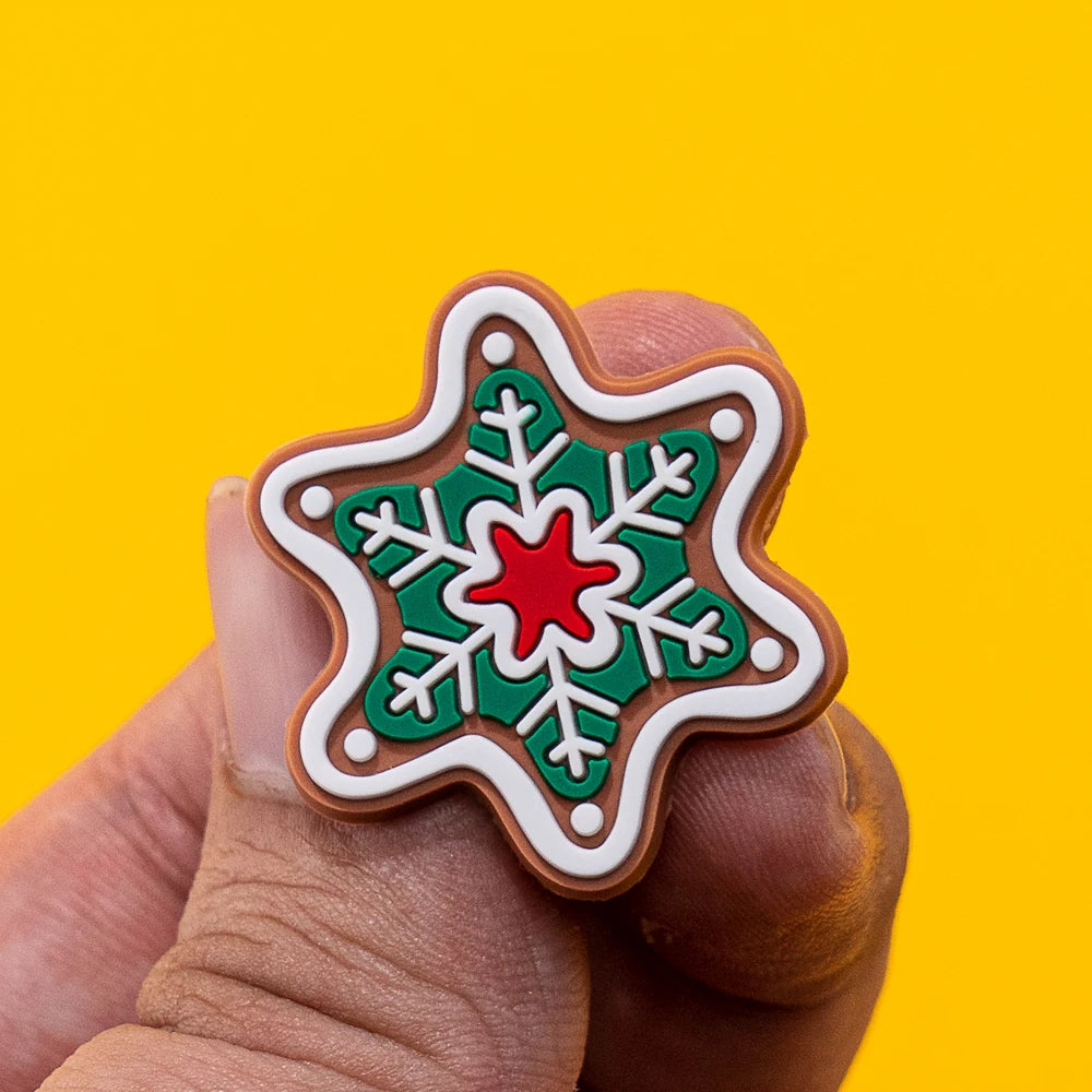Star-shaped shoe charm with green snowflake design and red center held by a hand against a yellow background