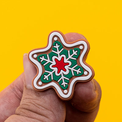 Star-shaped shoe charm with green snowflake design and red center held by a hand against a yellow background