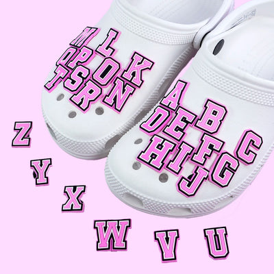 White clogs with pink lettering shoe charms on a pink background