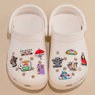 White clogs with 'Friends' themed pins on a beige background