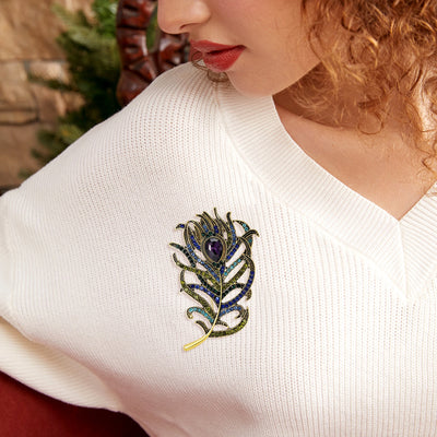 Woman wearing a white sweater with a decorative peacock feather brooch.