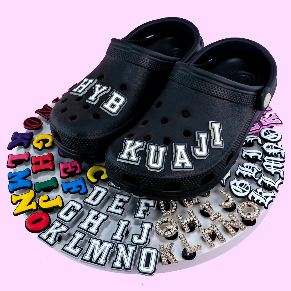 Black clogs with customizable letter charms on a pink background