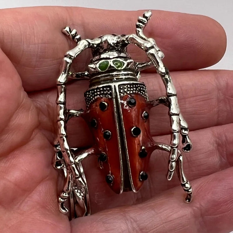 Red Metallic beetle brooch held in a hand against a neutral background