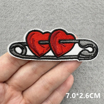 Embroidered patch with two red hearts and black text held by a hand on a gray background