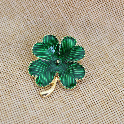 Green four-leaf clover brooch on a beige fabric background