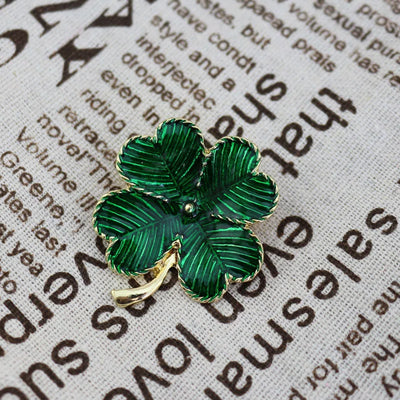 Green four-leaf clover brooch on a textured surface with text
