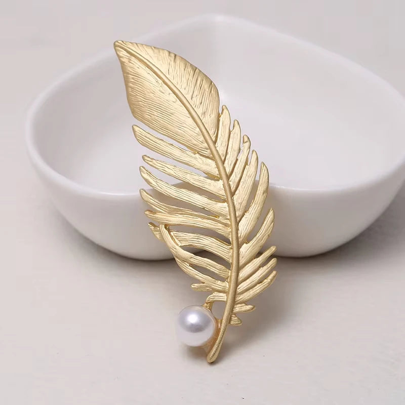 Gold leaf-shaped brooch with a pearl on a white dish