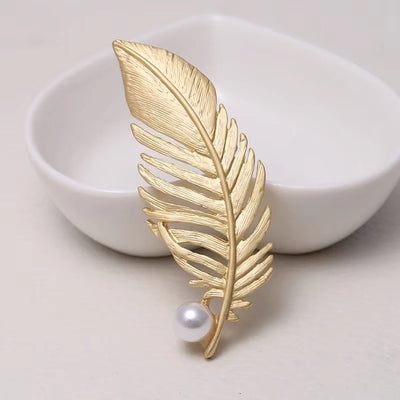 Gold leaf-shaped brooch with a pearl on a white dish