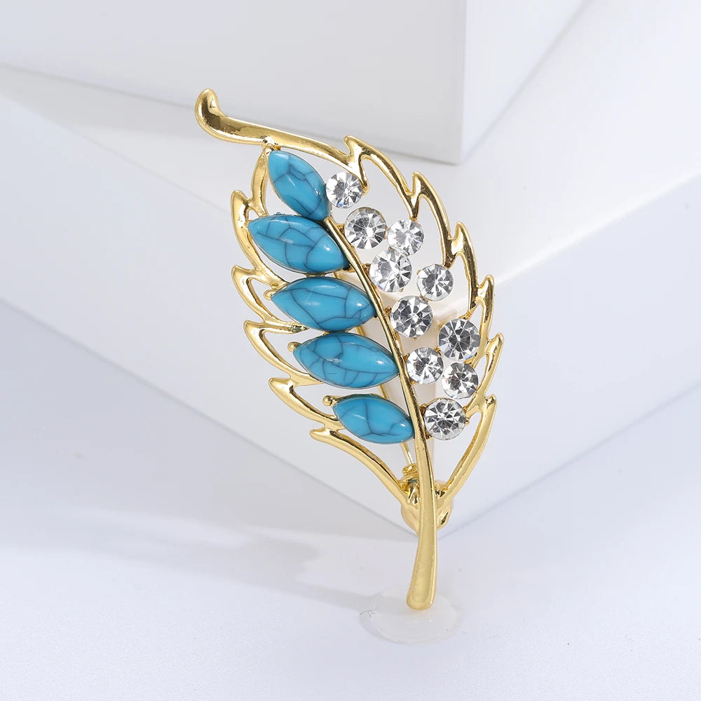 Gold leaf-shaped brooch with turquoise stones and clear crystals on a white background
