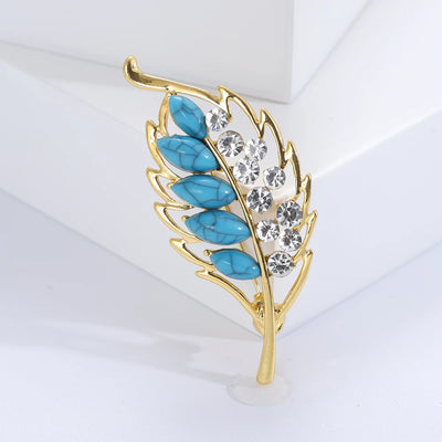Gold leaf-shaped brooch with turquoise stones and clear crystals on a white background