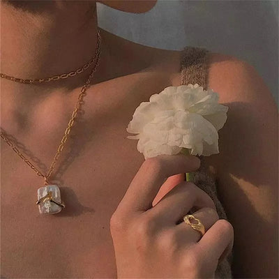 Person wearing gold jewelry Necklace of  a hands hugging a white Natural iridescent stone pendant with a white flower, against a neutral background