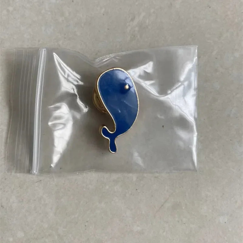 Blue whale-shaped pin in a clear plastic bag on a beige surface